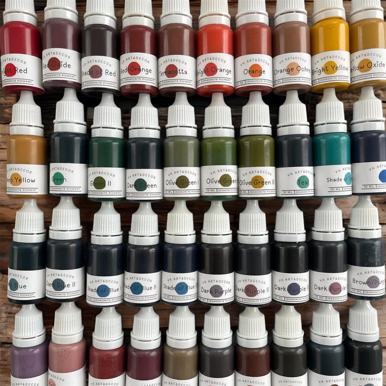May include: A collection of forty small plastic dropper bottles containing various colored pigments for Jesmonite. Each bottle features a white cap and a label displaying the brand name, color name, and a circular color swatch for identification.