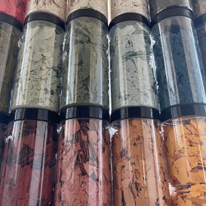 May include: Assortment of small glass jars filled with colorful flakes. The jars are arranged in a row, with the flakes visible through the clear glass.