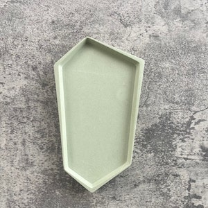 May include: A light green geometric tray with a hexagonal shape. The tray is made of concrete and has a smooth, matte finish.