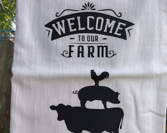 May include: White kitchen towel with black text that reads "Welcome to our Farm" and a black silhouette of a cow, pig, and rooster.