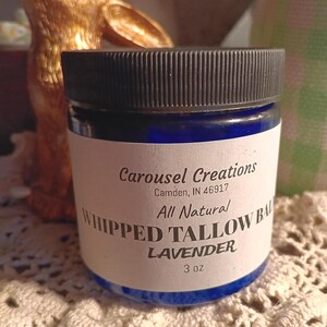 Può includere: Un barattolo blu con un'etichetta bianca che recita "Carousel Creations, Camden, IN 46917, All Natural, Whipped Tallow Balm Lavender, 3 oz."