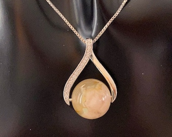 May include: A silver pendant necklace featuring a large, round, light-colored stone. The pendant has a teardrop design with a row of small, clear stones along the edges. The chain is a delicate silver box chain.