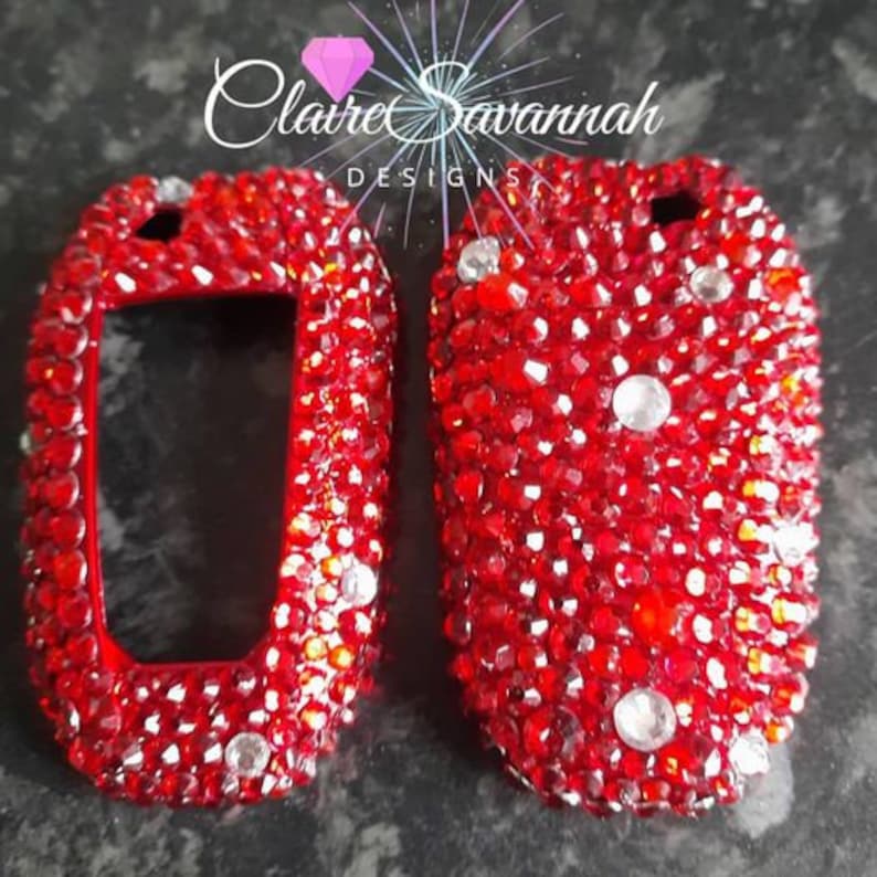 May include: Two red key fobs covered in red rhinestones. The key fobs are shaped like a car key and have a clear plastic window in the center.