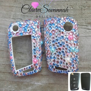 May include: Two white car key covers with a design of pink, blue, and white rhinestones. The key covers are shown next to the original car key.
