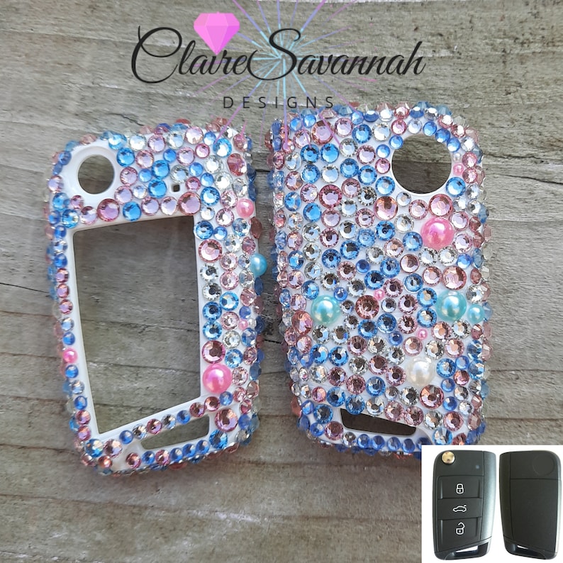 May include: Two white car key covers with a design of pink, blue, and white rhinestones. The key covers are shown next to the original car key.