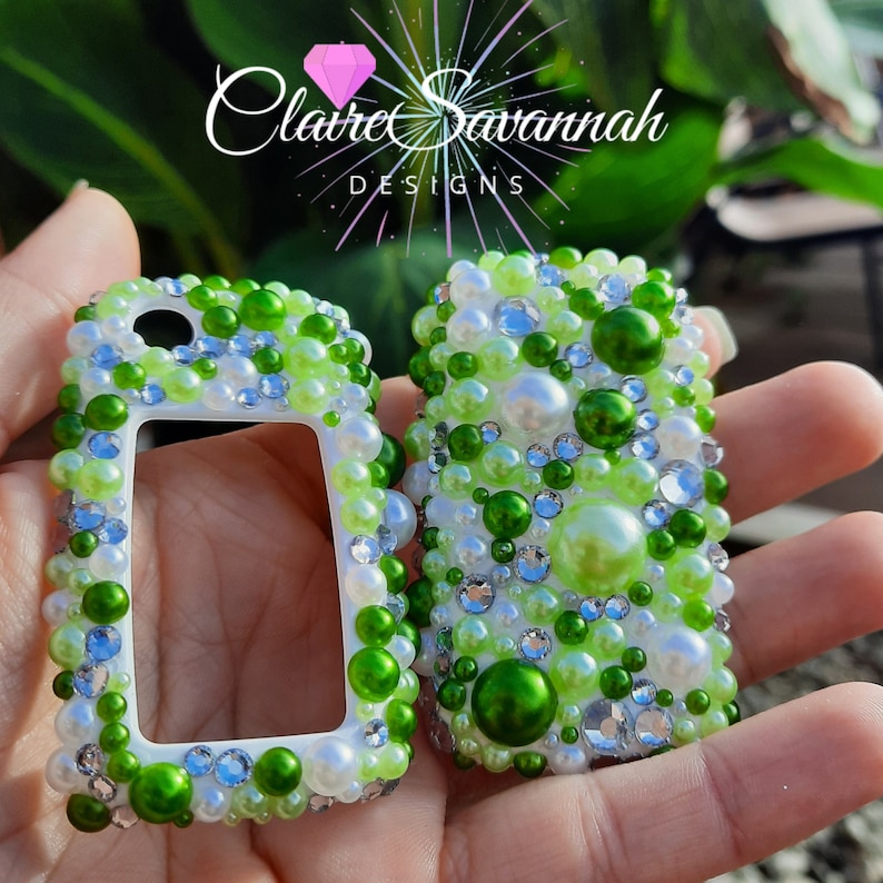 May include: Two white key fob covers with a green and white pearl design. The covers are decorated with green, white, and clear rhinestones. The text "Claire Savannah Designs" is visible in the background.
