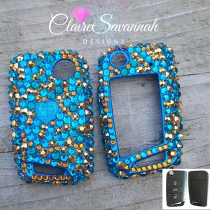 May include: Two blue and gold jeweled key fobs with a black key fob in the bottom right corner.  The key fobs are covered in rhinestones and have a clear plastic cover over the buttons.  The key fobs are for a car key.