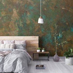 Puede incluir: Interior de dormitorio con cabecero de madera rústica, ropa de cama gris claro y una pared texturizada en tonos marrón, verde y azul. Una pequeña mesita auxiliar con jarrones blancos. Una lámpara colgante ilumina el espacio.