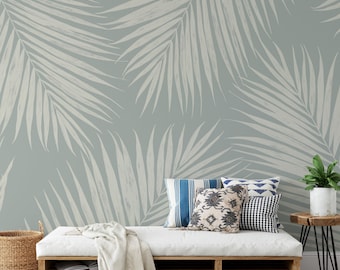May include: A light blue wall with a repeating pattern of white palm leaves. A white daybed with pillows and a blanket sits in front of the wall. A woven basket, a small wooden table, and a striped rug complete the scene.