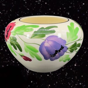 May include: Cream-colored ceramic bowl with a floral design. The bowl features red and purple flowers with green leaves. The interior of the bowl is a light yellow color. The flowers are painted in a watercolor style.