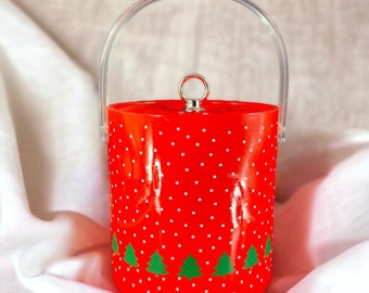 Könnte beinhalten: Roter Eiseimer mit weißen Punkten, einem durchsichtigen Plastikgriff und einem silbernen Deckel. Der Eimer hat ein grünes Weihnachtsbaumdesign am Boden.
