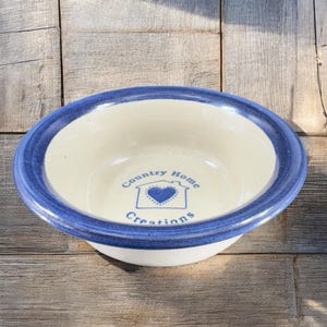 May include: A white ceramic bowl with a blue rim and a blue and white logo that says "Country Home Creations" with a house and heart design.