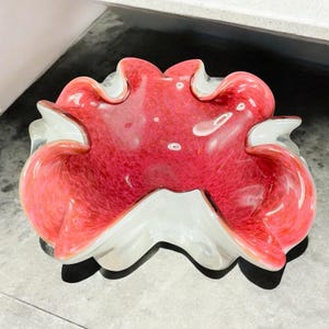 May include: A decorative glass bowl with a ruffled edge. The bowl features a vibrant red interior with white accents on the rim and exterior. The bowl's design is organic and flowing, with a glossy finish.