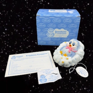 May include: A blue and white ceramic figurine of a baby bird sleeping on a cloud. The figurine is part of the Sonshine Promises collection and comes in a blue box with the company logo. The figurine is a baby girl and has a pink bow.