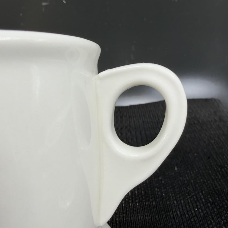 May include: A white ceramic mug with a black handle and the text "But First, Coffee" in a handwritten style. The mug is on a white surface. The mug is approximately 4 inches tall.