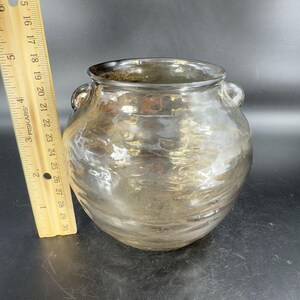 May include: A clear glass vase with a textured surface and two small handles on the sides. The vase has a rounded body and a wide opening.