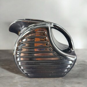 May include: A black ceramic pitcher with a ribbed design and a handle. The pitcher has a glossy finish.