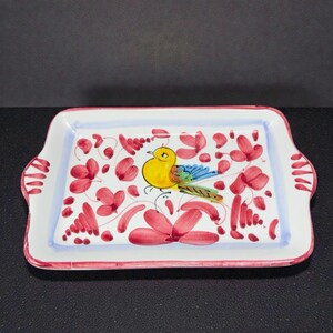May include: Rectangular ceramic serving tray with a hand-painted design. The tray features a yellow bird with blue and green wings, surrounded by red floral accents on a white background. The rim is outlined in red.