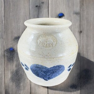 May include: White ceramic jar with a blue heart and paw prints. The jar has a round shape and a smooth, textured surface. The jar has a label that says "Crooked Valley".