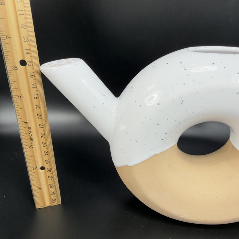 Peut inclure: Une th&eacute;i&egrave;re en c&eacute;ramique blanche et beige avec une anse et un bec verseur. La th&eacute;i&egrave;re mesure environ 25 cm de diam&egrave;tre. Une r&egrave;gle en bois est plac&eacute;e &agrave; c&ocirc;t&eacute; de la th&eacute;i&egrave;re.
