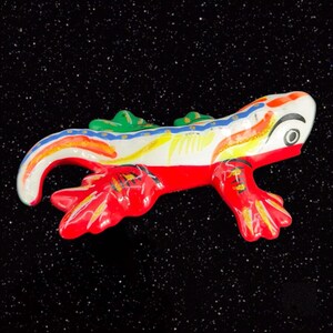 May include: A hand-painted ceramic lizard figurine with red, white, green, blue, and yellow accents. The lizard is in a curled position with its tail curled around its body.
