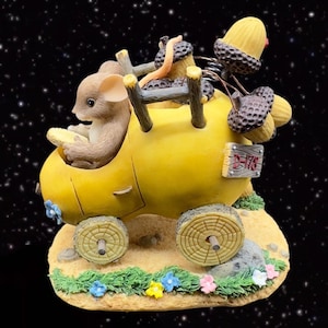 May include: A yellow acorn-shaped car with two mice passengers. The car has a wooden sign that says "D-178". The car is on a brown base with green grass and flowers.
