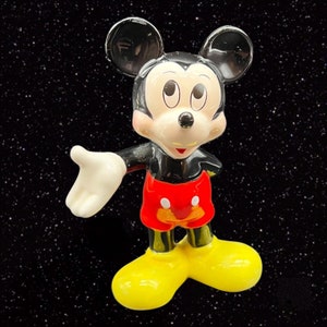Puede incluir: Una figurita de cer&aacute;mica negra y roja de Mickey Mouse con orejas grandes, una amplia sonrisa y una camisa de lunares rojos y blancos. La figurita est&aacute; de pie sobre un fondo negro.