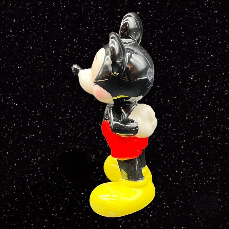 Puede incluir: Una figurita de cer&aacute;mica negra y roja de Mickey Mouse. Mickey est&aacute; de pie con la mano derecha en la cadera y la mano izquierda levantada. Lleva zapatos amarillos.