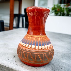 May include: A red, brown, blue, and white ceramic vase with a geometric pattern. The vase has a wide base and a narrow neck.