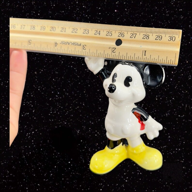 K&ouml;nnte beinhalten: Eine wei&szlig;e Keramikfigur von Mickey Mouse mit schwarzen Ohren und Schuhen. Mickey tr&auml;gt rote Shorts und hat einen schwarzen Umriss um die Augen. Er steht mit erhobenem rechten Arm und dem linken Arm an seiner Seite. Die Figur ist etwa 12,7 cm hoch.