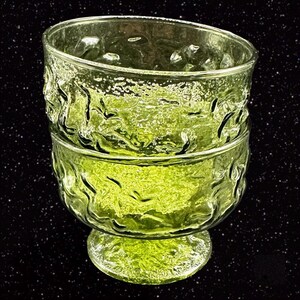 May include: Two stacked green glass bowls with a textured, wavy design. The bowls are clear and have a slight green tint. The bowls are on a black background.