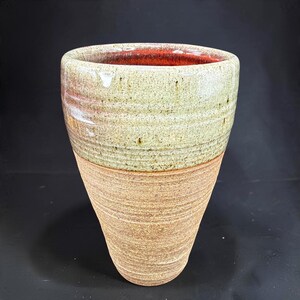 May include: A tapered ceramic tumbler featuring a textured, unglazed brown base with horizontal ridges and a smooth, speckled light green glazed upper section. The interior of the vessel is finished with a vibrant, glossy red glaze.