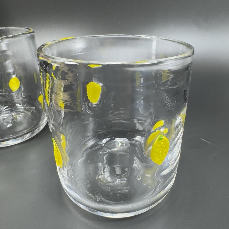 May include: Two clear drinking glasses with yellow lemon designs. The glasses are cylindrical with a slightly textured surface. The yellow lemon designs are scattered around the glass, adding a touch of whimsy. Perfect for serving beverages.