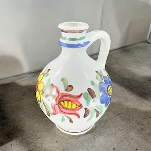 May include: White ceramic pitcher with a handle, decorated with hand-painted flowers in shades of yellow, red, blue, and green.