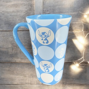 May include: A blue ceramic mug with a white polka dot pattern and a blue Stitch character from Lilo & Stitch on each dot.