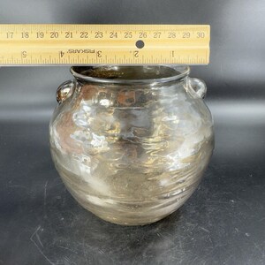 May include: A large, clear glass vase with a metallic finish. The vase has two handles and a rounded body. The vase is approximately 8 inches tall.