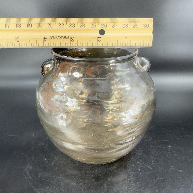 May include: A large, clear glass vase with a metallic finish. The vase has two handles and a rounded body. The vase is approximately 8 inches tall.