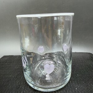 May include: A clear glass cylinder vase with a white rim and lavender heart-shaped designs. The vase is approximately 15 cm tall and has a simple, elegant design, suitable for various floral arrangements.