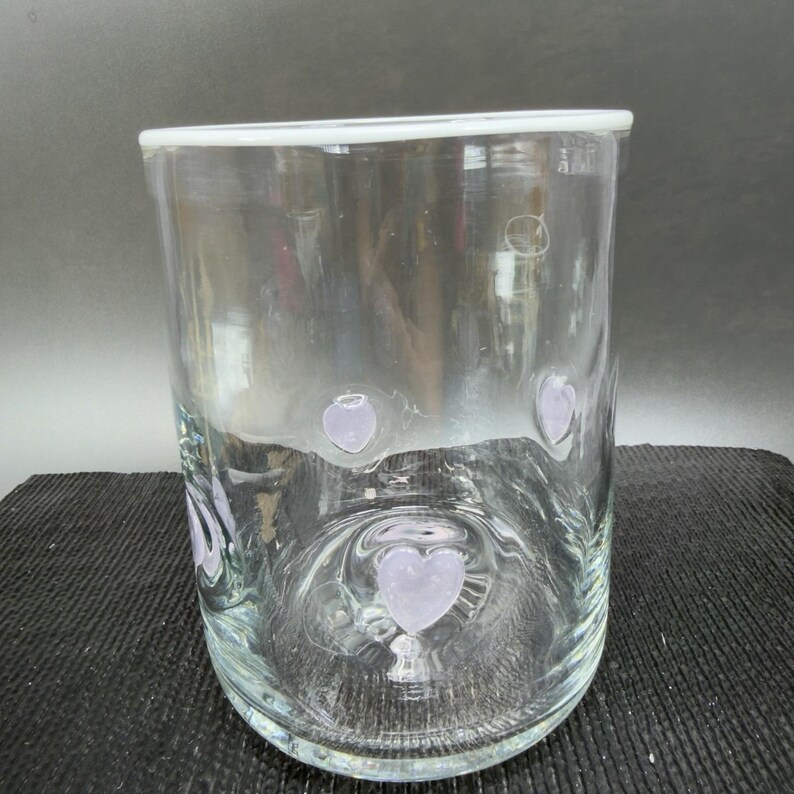 May include: A clear glass cylinder vase with a white rim and lavender heart-shaped designs. The vase is approximately 15 cm tall and has a simple, elegant design, suitable for various floral arrangements.