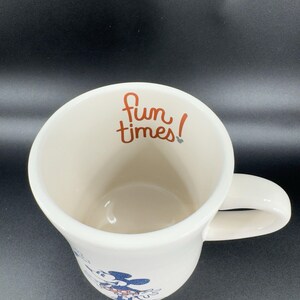 May include: White ceramic mug with a blue and red illustration of Mickey Mouse and Minnie Mouse. The mug has a handle and says "Fun times!" in orange lettering.