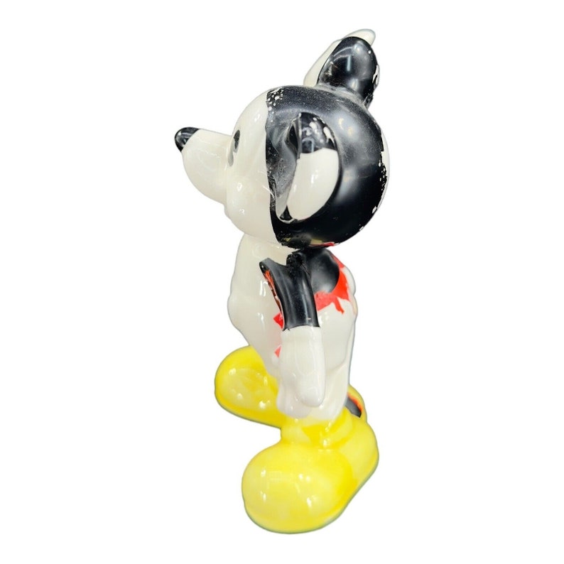 K&ouml;nnte beinhalten: Eine Keramikfigur von Mickey Mouse, die mit den Armen an den Seiten steht. Er tr&auml;gt seine charakteristischen roten Shorts, gelbe Schuhe und schwarz-wei&szlig;e Handschuhe. Die Figur ist wei&szlig; mit schwarzer Farbe f&uuml;r seine Ohren, sein Gesicht und seine Handschuhe.