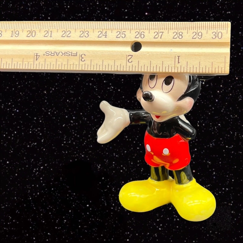 Puede incluir: Una figurita de cer&aacute;mica de Mickey Mouse, de pie con el brazo derecho extendido y la mano izquierda en la cadera. Lleva sus caracter&iacute;sticos pantalones cortos rojos con lunares blancos, zapatos negros y guantes blancos. La figurita mide aproximadamente 10 cm de alto.