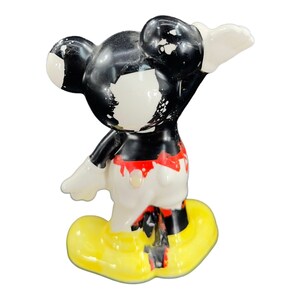 K&ouml;nnte beinhalten: Eine vintage Keramik-Figur von Mickey Mouse mit schwarzer, wei&szlig;er, roter und gelber Farbe. Die Figur steht mit einem erhobenen Arm und ist leicht abgebrochen.
