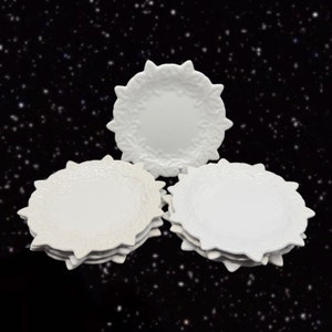May include: A set of six white ceramic plates with a decorative floral design around the edge. The plates are stacked in two groups of three.