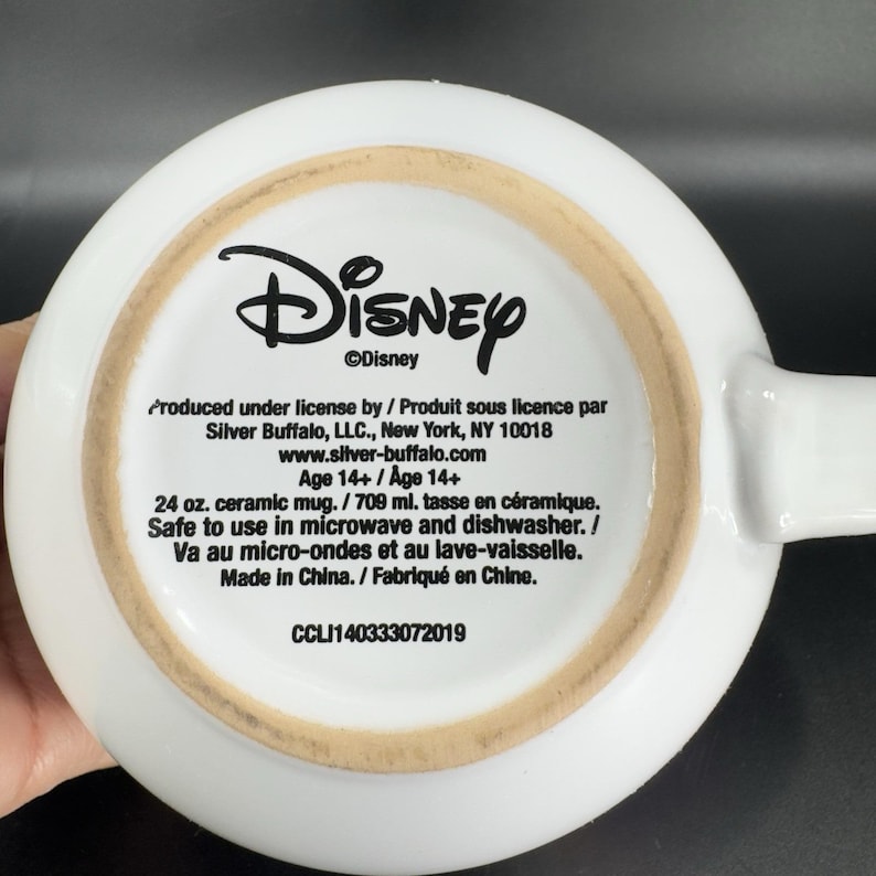 May include: White ceramic mug with a Disney logo and product information. The mug is 24 ounces and is safe for use in the microwave and dishwasher. It is made in China.