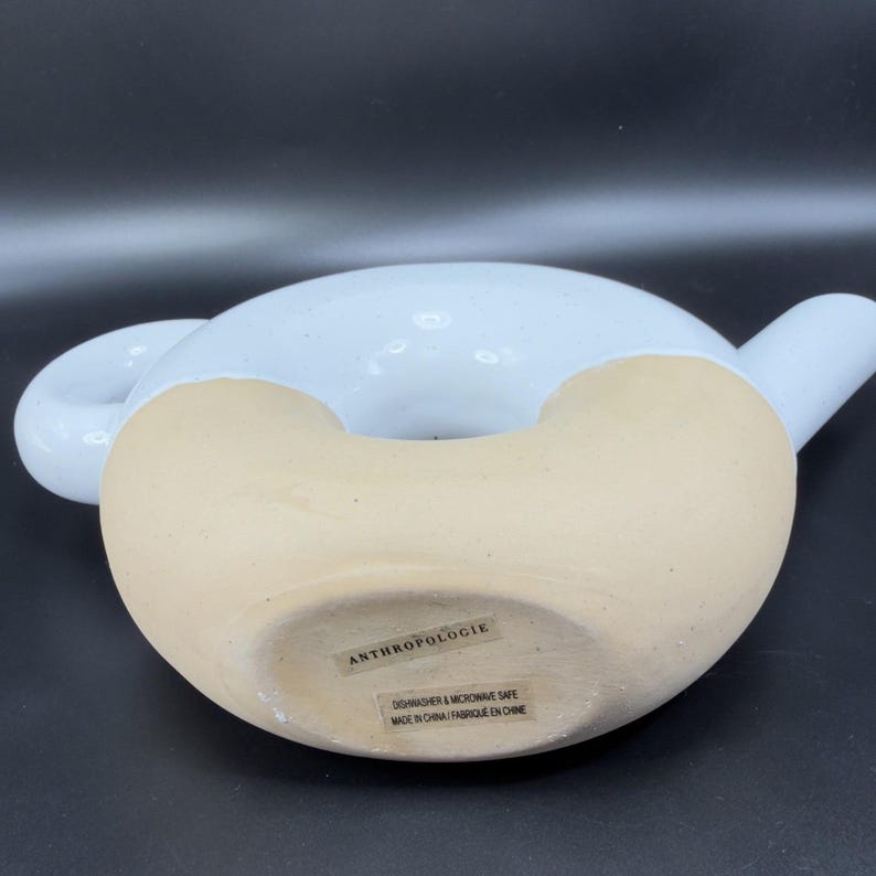 Peut inclure: Une th&eacute;i&egrave;re en c&eacute;ramique avec un dessus &eacute;maill&eacute; bleu clair et une base beige. La th&eacute;i&egrave;re a une forme arrondie avec une anse et un bec. Le fond de la th&eacute;i&egrave;re porte une &eacute;tiquette indiquant "ANTHROPOLOGIE" et "DISHWASHER & MICROWAVE SAFE MADE IN CHINA/FABRIQUE EN CHINE."