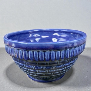 May include: A deep blue ceramic bowl with a textured, basket-weave design. The bowl has a wide, rounded rim and a slightly flared base. The exterior features vertical and horizontal lines, creating a grid-like pattern. The bowl is likely for serving or display.