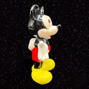 Puede incluir: Una figurita de cer&aacute;mica en blanco y negro de Mickey Mouse con pantalones cortos rojos y zapatos amarillos. La figurita est&aacute; de pie sobre un fondo negro.