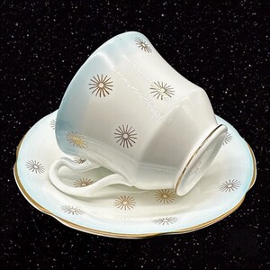 May include: A white teacup and saucer with a blue rim and gold starburst pattern.