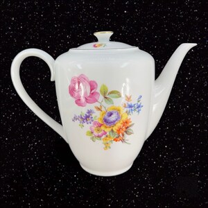 May include: White porcelain teapot with a floral design featuring pink, yellow, purple, and blue flowers. The teapot has a gold trim around the lid.
